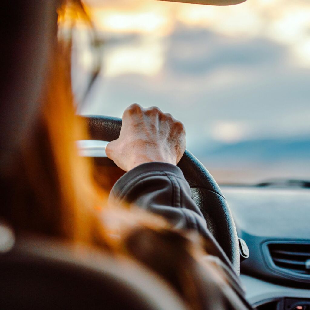 A woman drives a luxury rental car into the sunset.