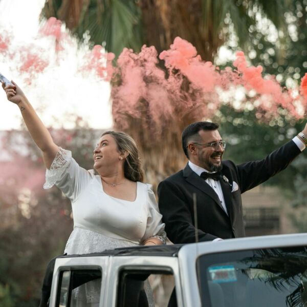 At a wedding ceremony, a luxury car pulls away with the bride and groom.