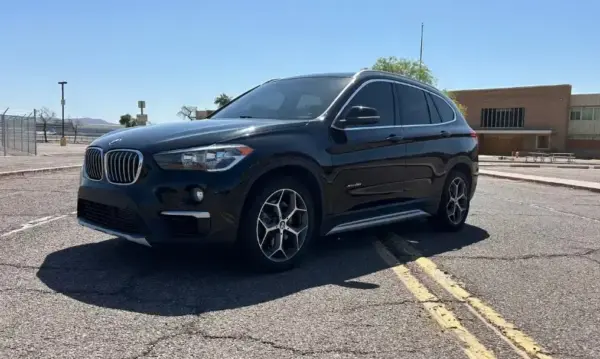 Black BMW SUV parked in a paved lot on a sunny day, shown in a three-quarter front view with yellow parking lines nearby.