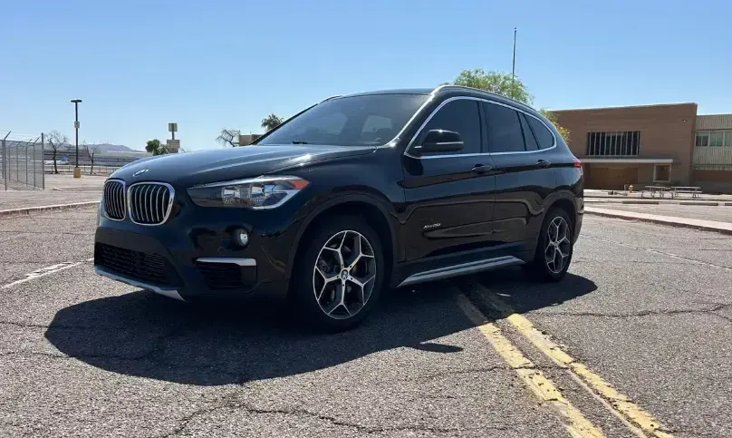Black BMW SUV parked in a paved lot on a sunny day, shown in a three-quarter front view with yellow parking lines nearby.