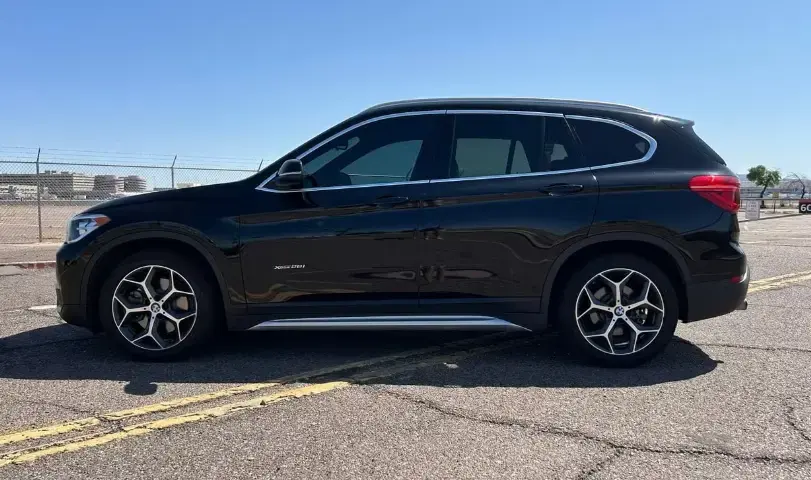 Side view of a black BMW SUV parked in an empty lot, showing silver alloy wheels and chrome trim.