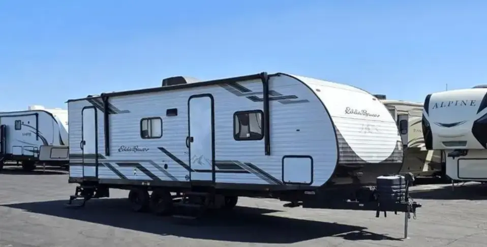 White travel trailer with gray and black graphics parked in an RV lot, with other campers visible in the background.