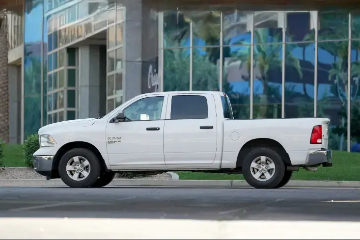 White extended-cab pickup truck parked on a city street in front of a glass-fronted building.