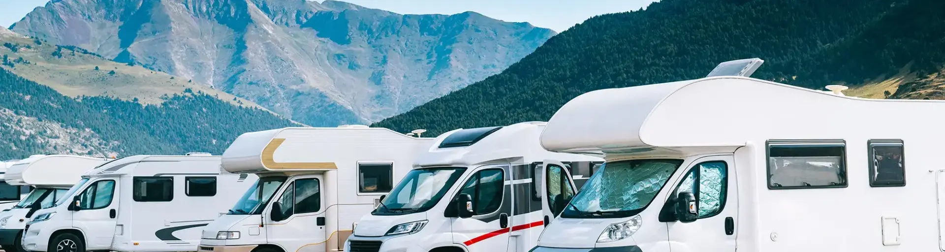 White motorhomes lined up in a parking area against a backdrop of blue mountains.