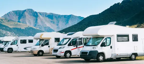White motorhomes lined up in a parking area against a backdrop of blue mountains.